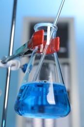 Photo of Laboratory analysis. Dripping blue liquid into flask on stand indoors, closeup