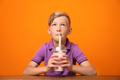 Photo of Little boy with cup of milk shake at table on color background