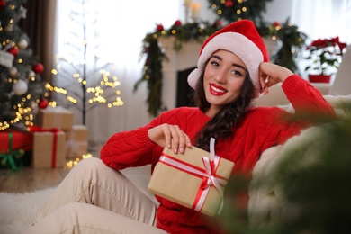 Beautiful woman wearing Santa hat with Christmas gift on floor at home