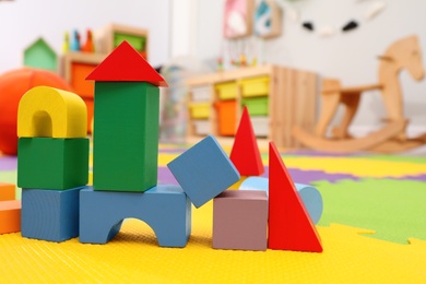 Photo of Wooden castle made of colorful blocks on carpet in playroom. Interior design