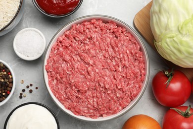 Minced meat in bowl and other ingredients for stuffed cabbage rolls on light grey table, flat lay