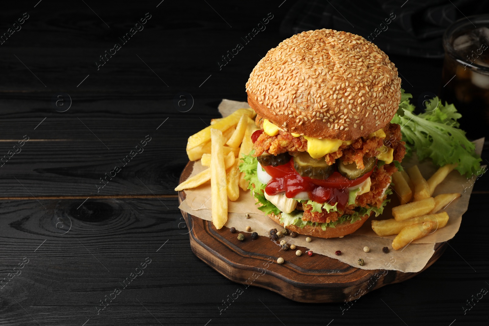 Photo of Delicious burger with crispy chicken patty and french fries on black wooden table. Space for text