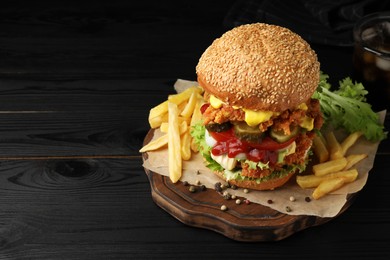 Photo of Delicious burger with crispy chicken patty and french fries on black wooden table. Space for text