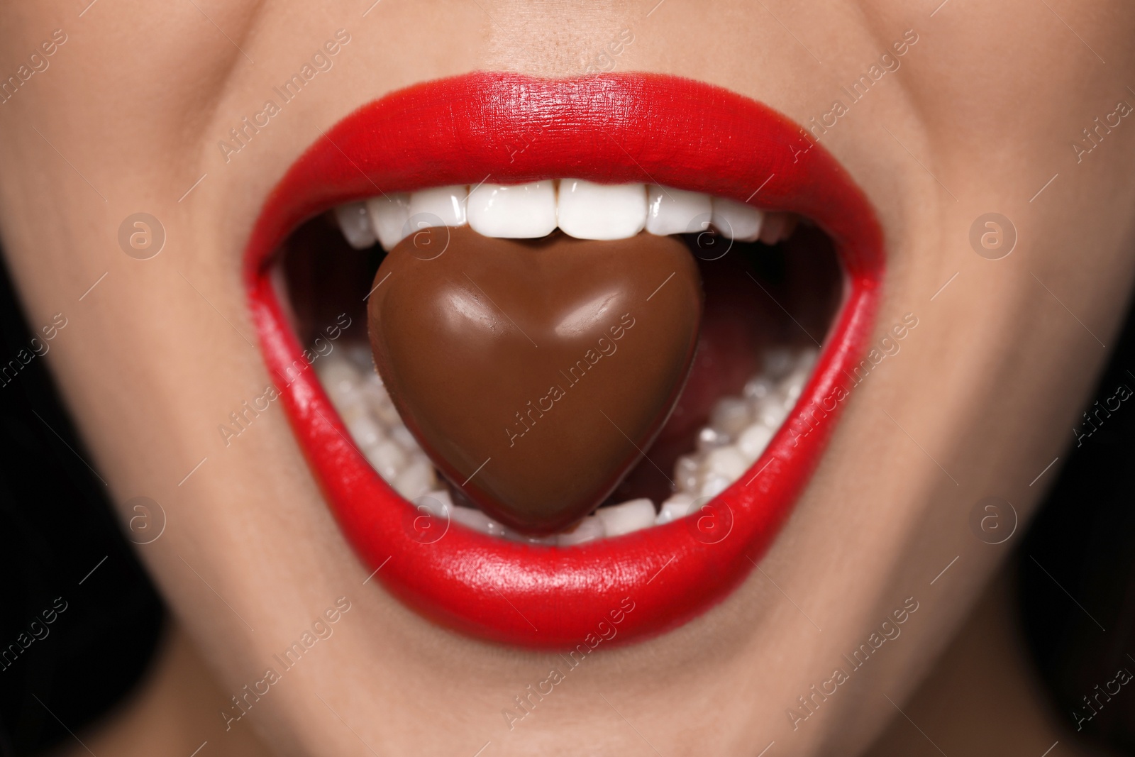 Photo of Young woman with red lips eating heart shaped chocolate candy, closeup