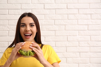 Photo of Young woman eating tasty burger near brick wall. Space for text