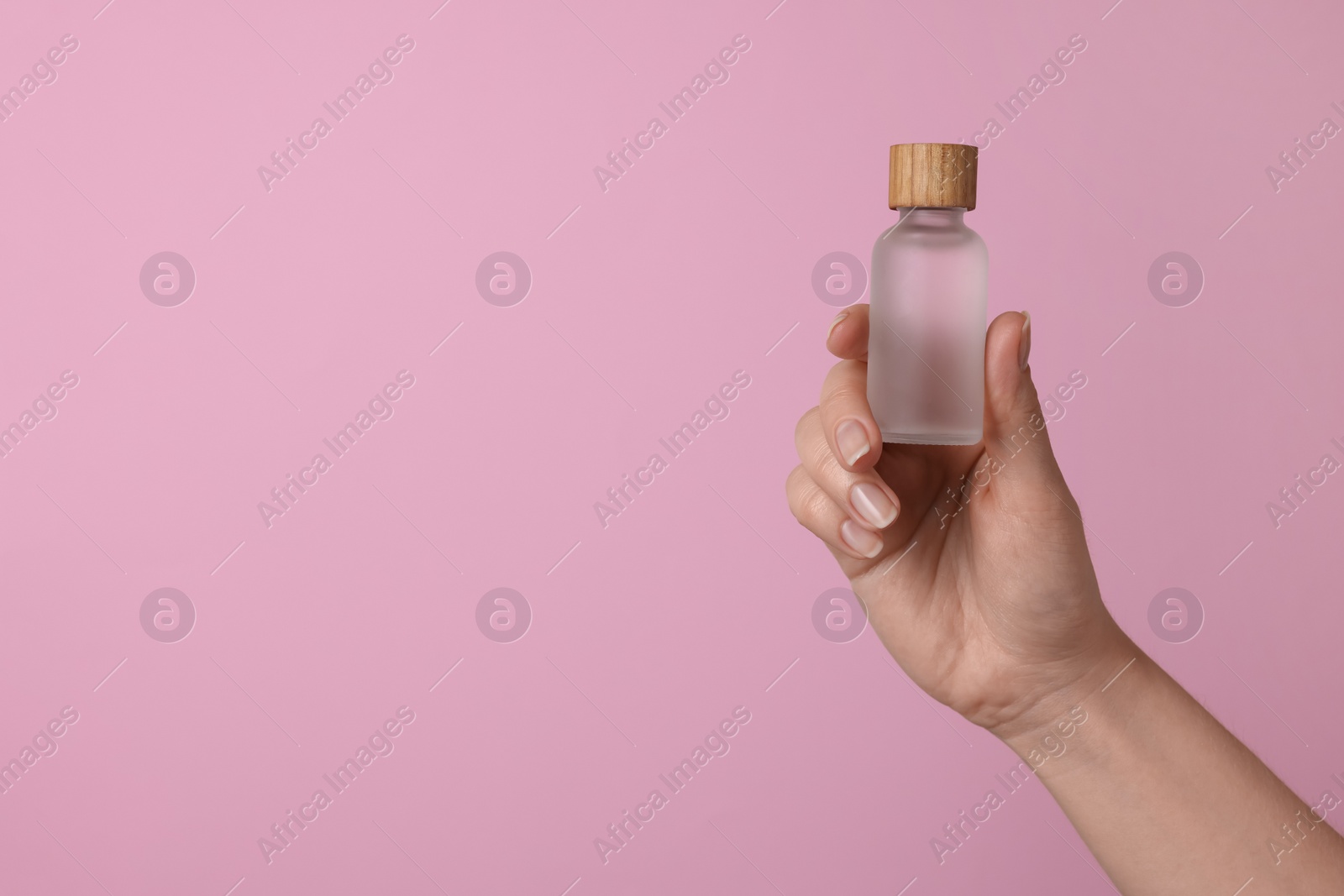 Photo of Woman holding bottle of cosmetic product on pink background, closeup. Space for text