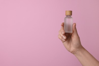 Woman holding bottle of cosmetic product on pink background, closeup. Space for text