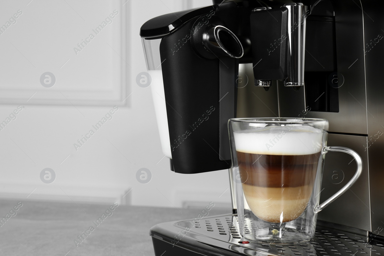 Photo of Modern coffee machine with glass cup of latte on grey table near white wall, closeup. Space for text