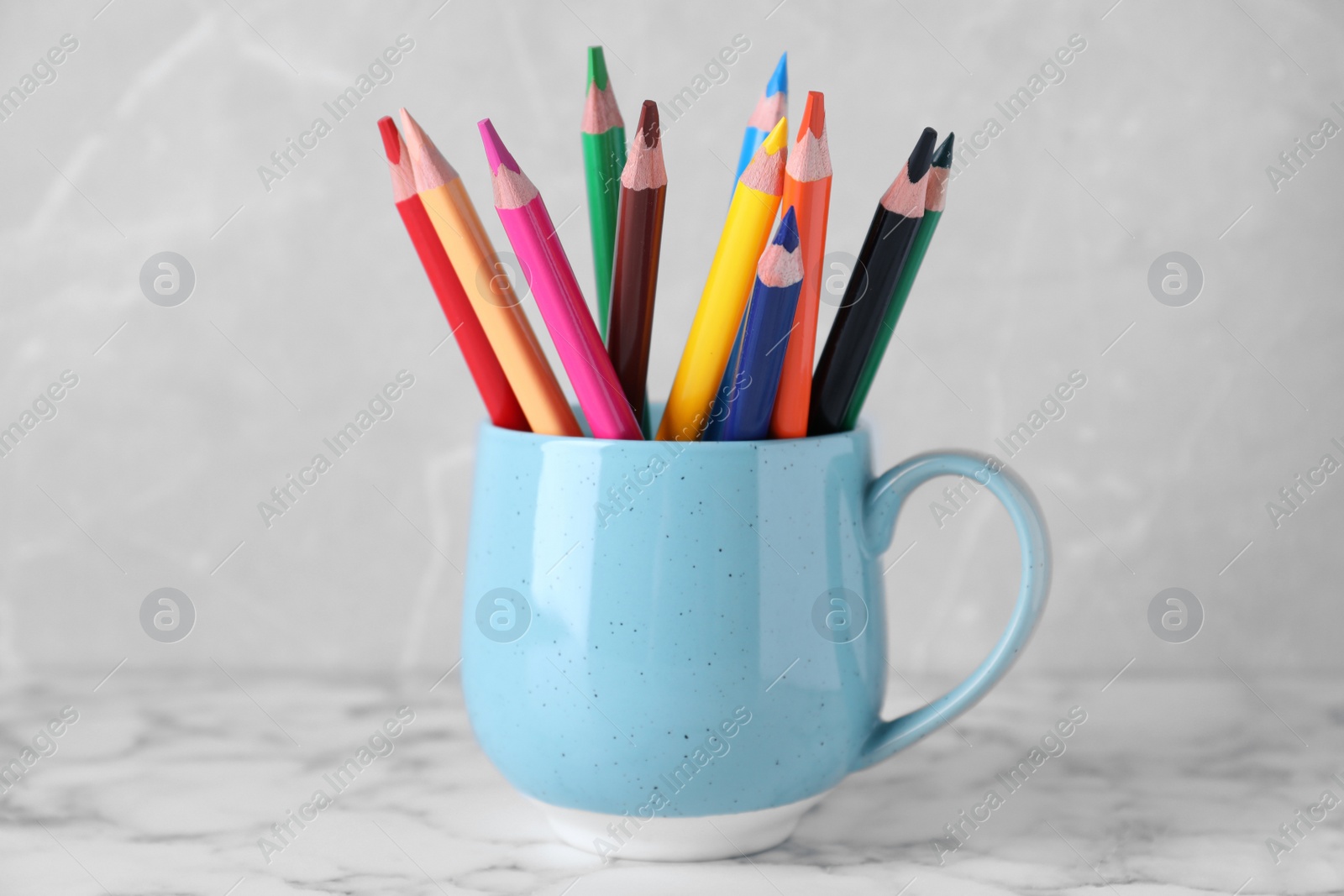 Photo of Colorful pencils in cup on white marble table against grey background