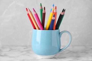 Photo of Colorful pencils in cup on white marble table against grey background