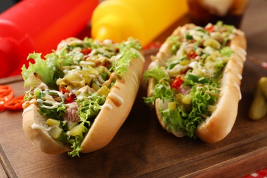 Photo of Tasty hot dogs with chili, lettuce, pickles and sauces served on wooden table, closeup