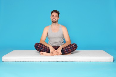 Photo of Smiling man sitting on soft mattress against light blue background