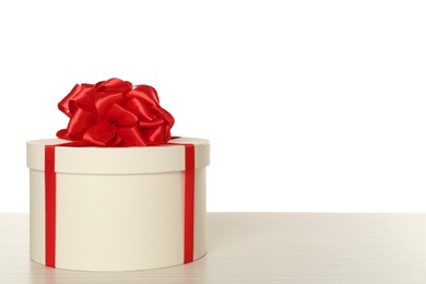 Round gift box with red bow on wooden table against white background, space for text