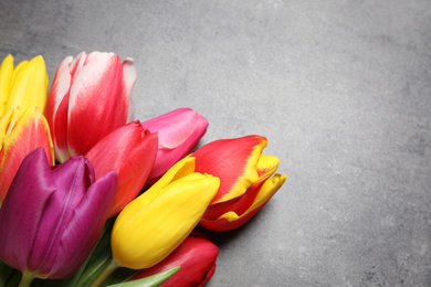 Photo of Beautiful spring tulips on grey stone table, above view. Space for text