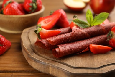 Photo of Delicious fruit leather rolls and strawberries on wooden table, closeup