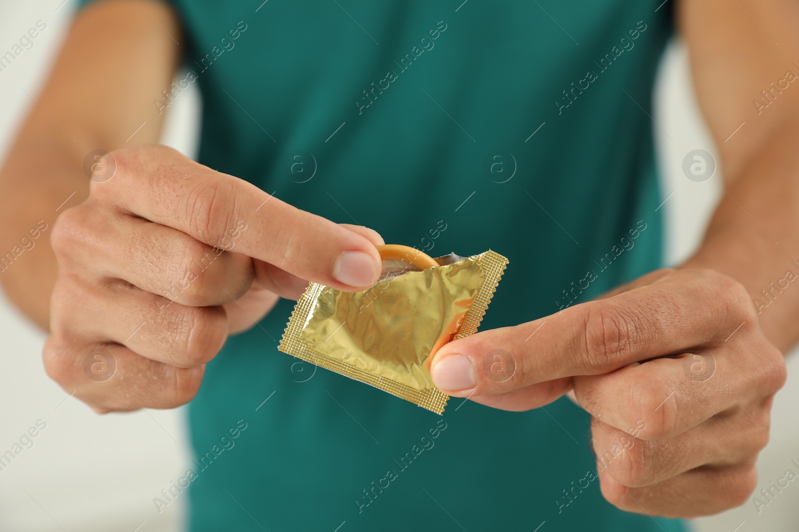 Photo of Young man holding condom on light background, closeup. Safe sex concept