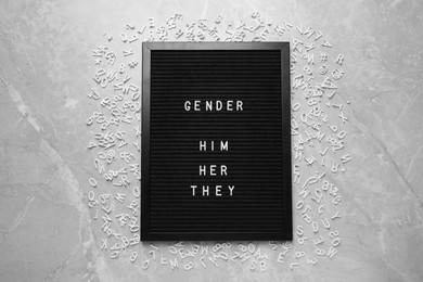 Photo of Black board with words Gender, Him, Her, They and letters on grey marble table, flat lay