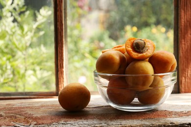 Photo of Glass bowl and delicious ripe apricots on wooden table near window. Space for text