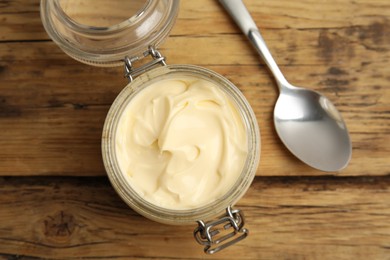 Photo of Jar of delicious mayonnaise and spoon on wooden table, flat lay