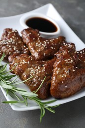 Photo of Glazed chicken wings, rosemary and soy sauce on grey table, closeup