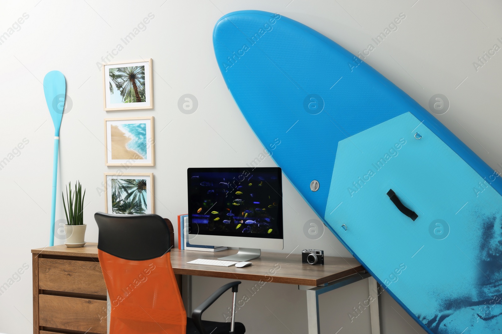 Photo of Stylish workplace with modern computer and SUP board near light wall in room. Interior design