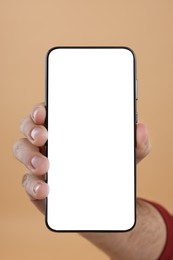 Photo of Man holding smartphone with blank screen on beige background, closeup