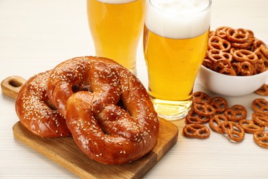 Photo of Tasty pretzels, crackers and glasses of beer on white wooden table
