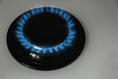 Photo of Gas burner with blue flame on modern stove, closeup