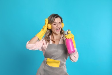 Photo of Beautiful young woman with headphones and bottle of detergent singing on light blue background