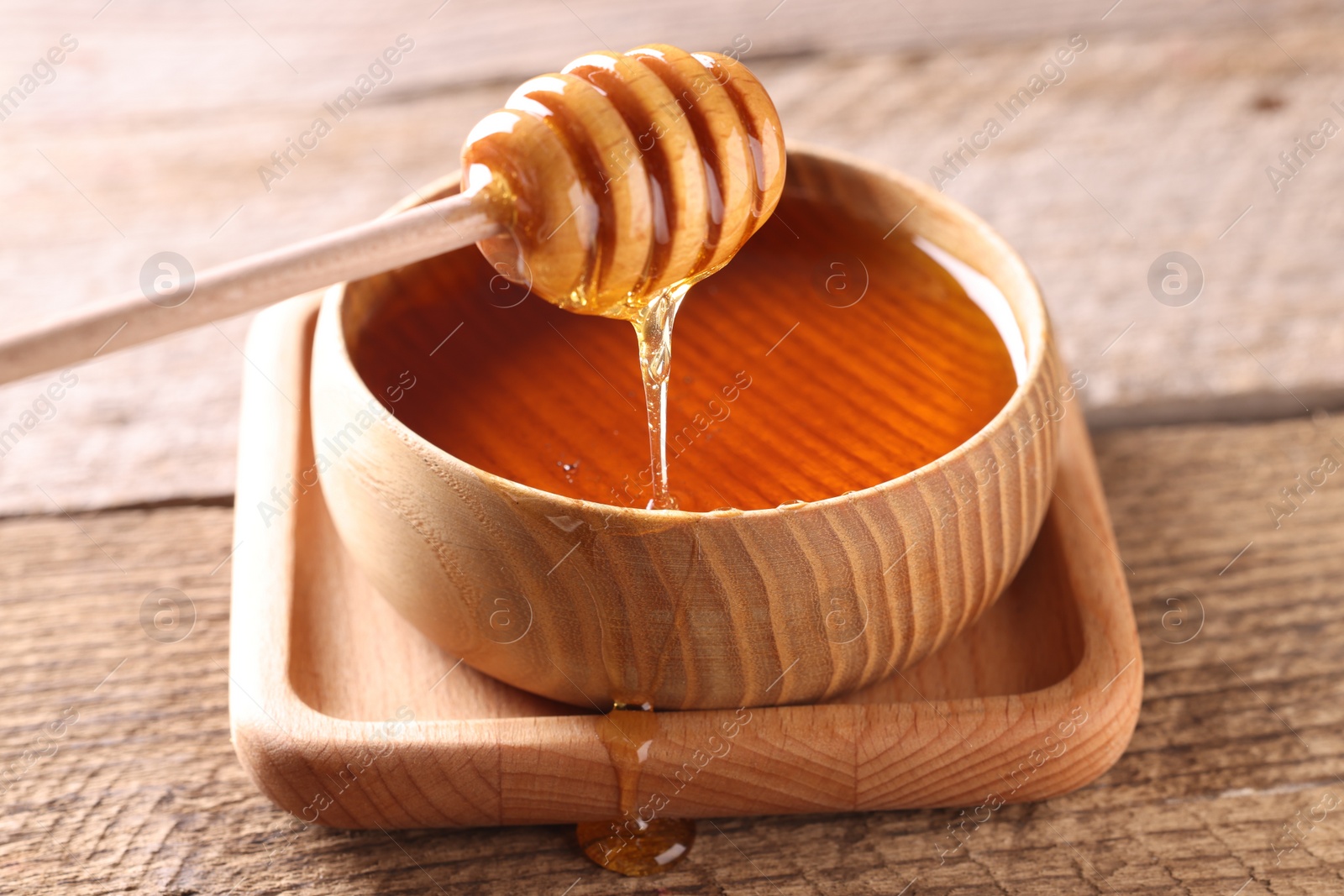 Photo of Pouring delicious honey from dipper into bowl on wooden table, closeup