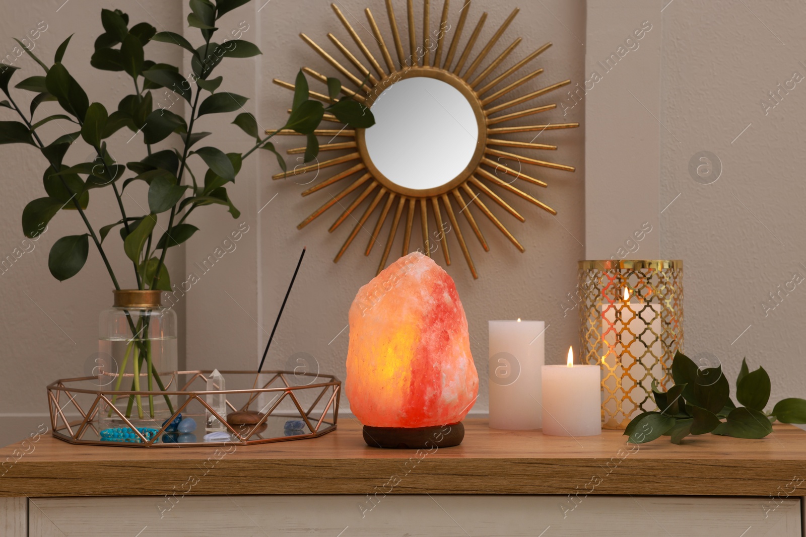 Photo of Himalayan salt lamp, candles and crystals on table near white wall indoors