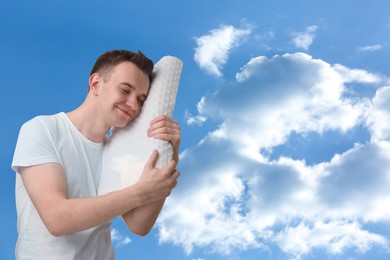 Man with orthopedic pillow against blue sky, space for text