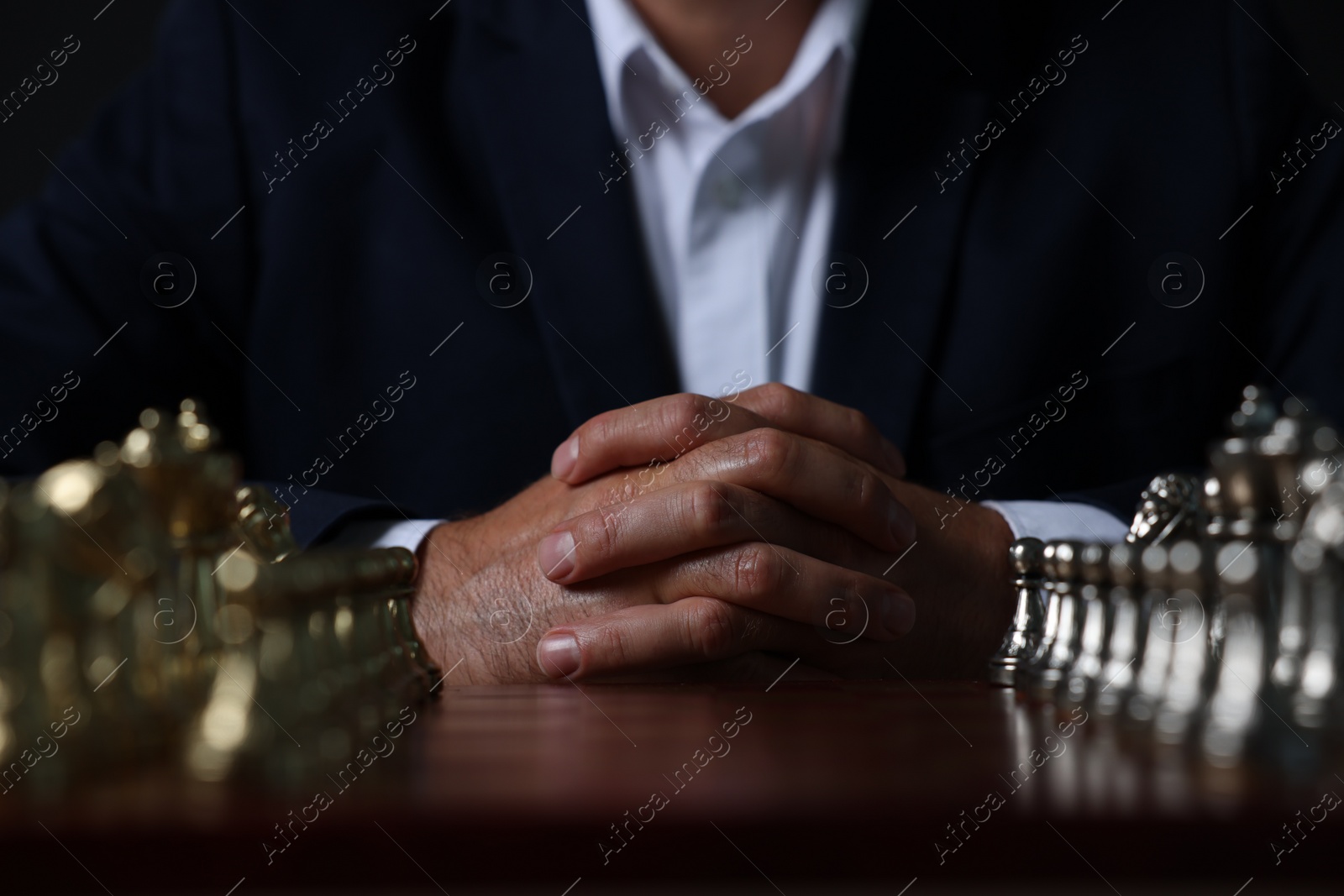 Photo of Man with chess pieces on board before game against dark background, closeup
