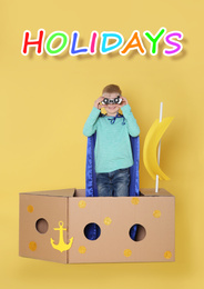 Image of School holidays. Cute little child playing with cardboard ship near yellow wall