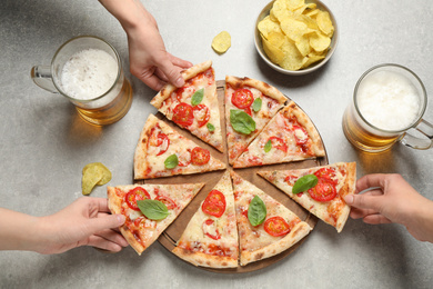 People taking slices of delicious pizza Margherita at light grey table, closeup