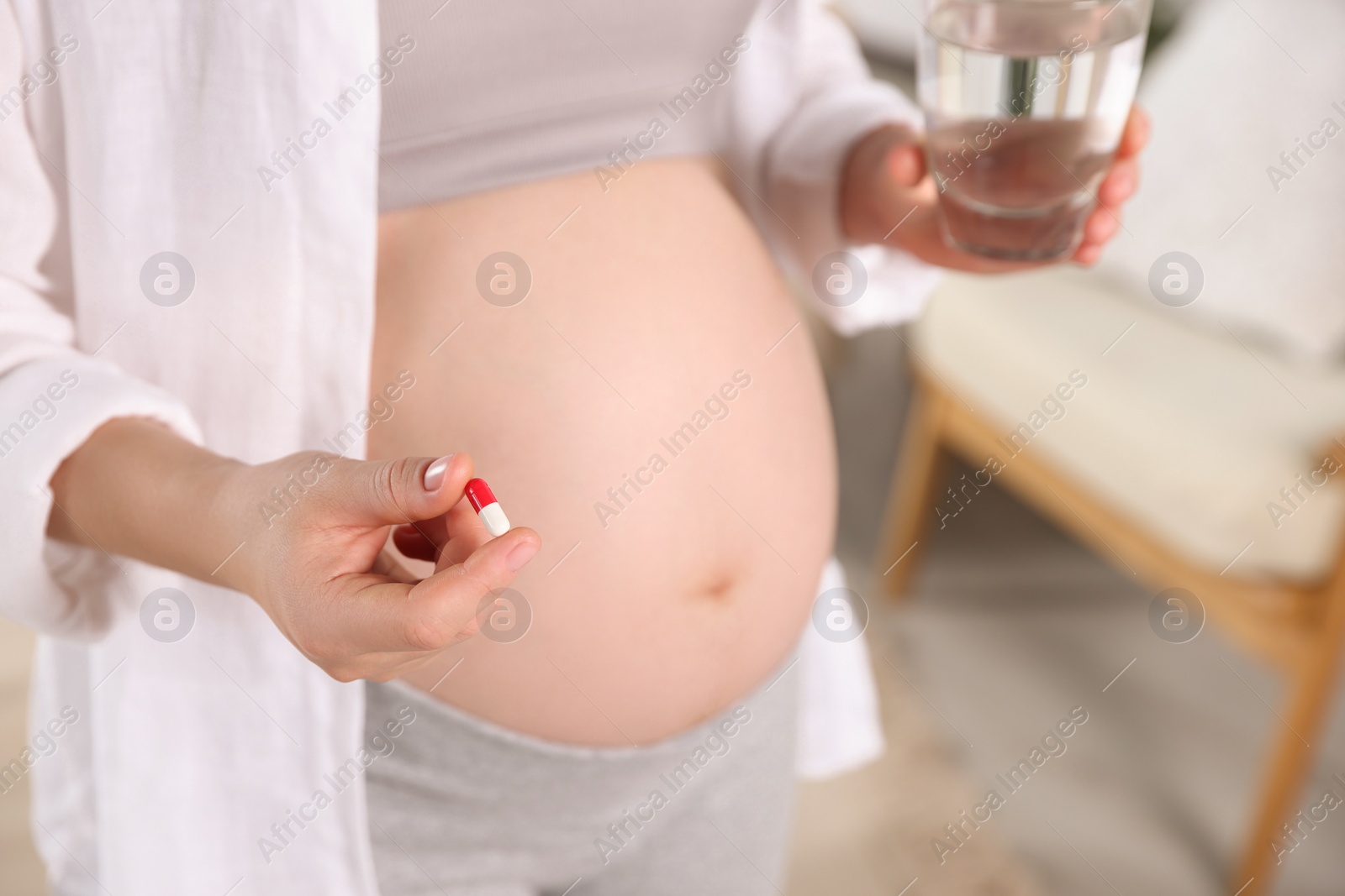 Photo of Pregnant woman holding pill and glass of water indoors, closeup