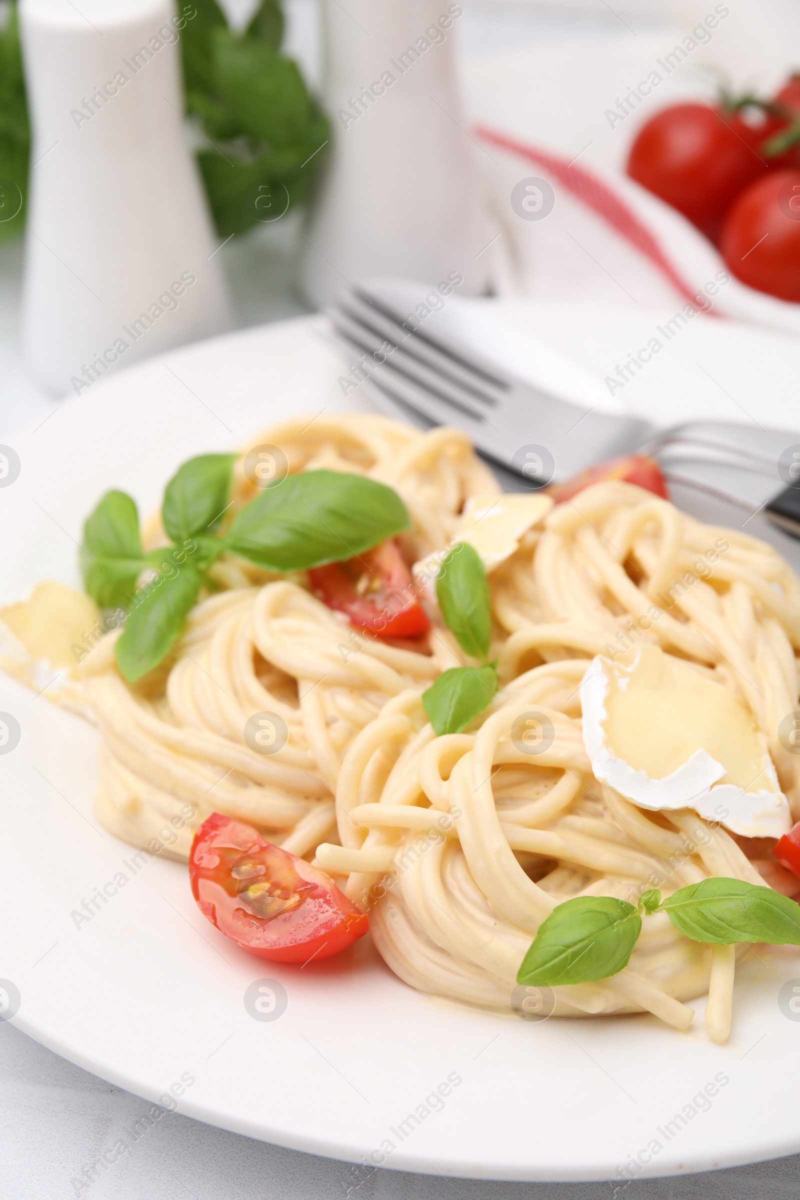 Photo of Delicious pasta with brie cheese, tomatoes, basil and cutlery on white table, closeup