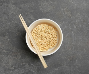 Cup of instant noodles with chopsticks on grey background, top view