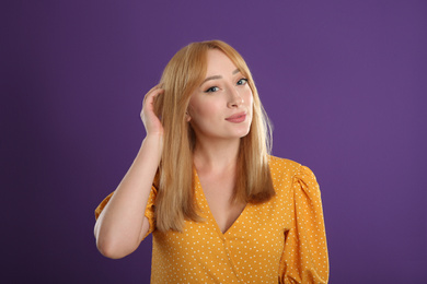 Beautiful young woman with blonde hair on purple background