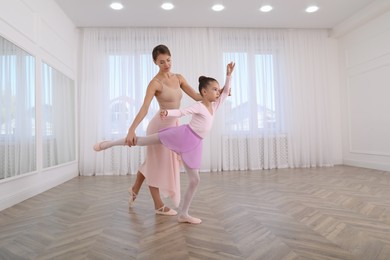 Photo of Little ballerina and her teacher practicing dance moves in studio. Space for text 