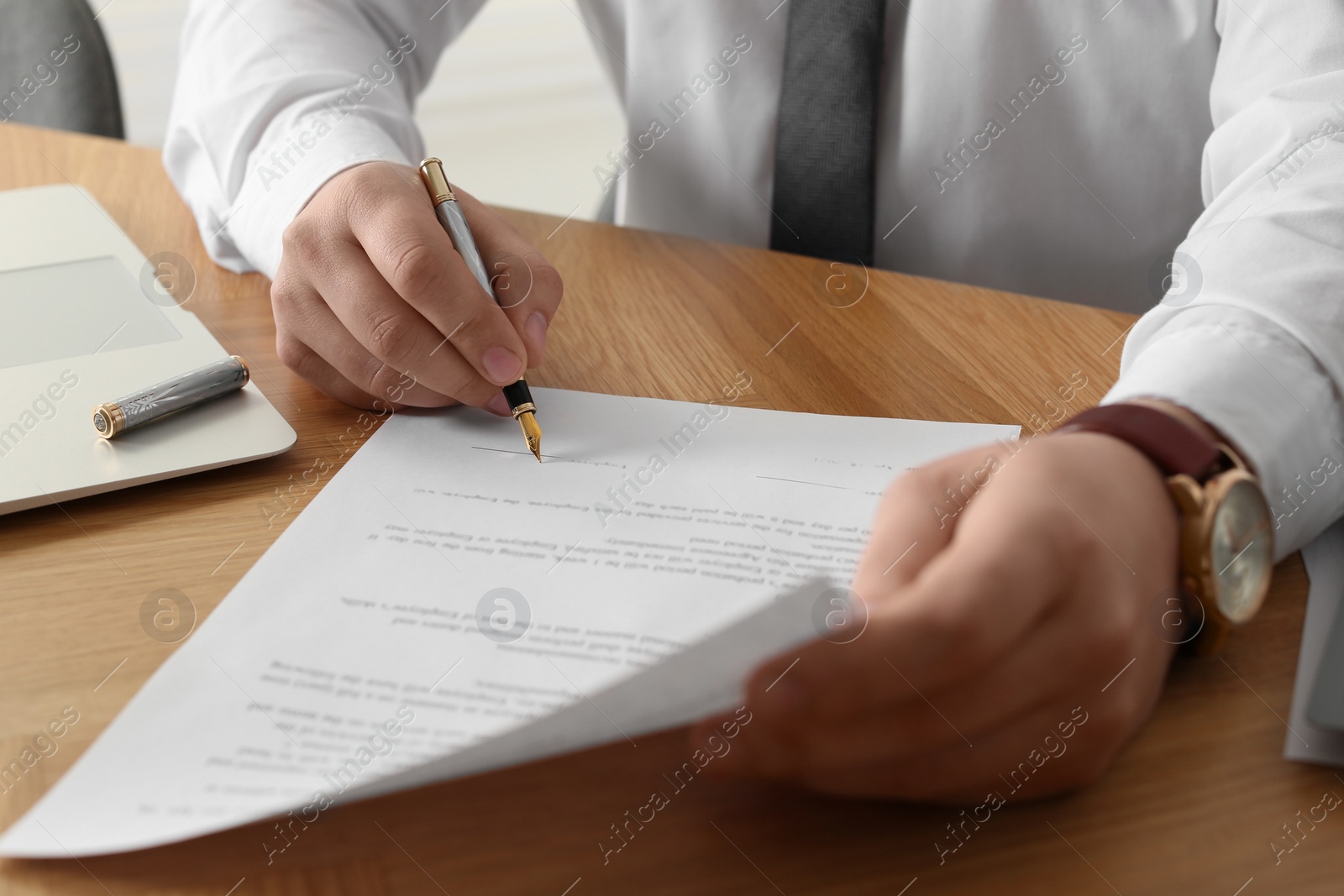 Photo of Notary signing document at wooden table, closeup