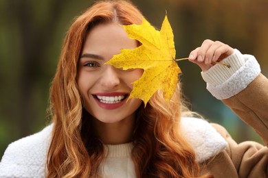 Photo of Portrait of smiling woman covering eye with autumn leaf outdoors