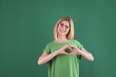 Portrait of woman making heart with her hands on color background