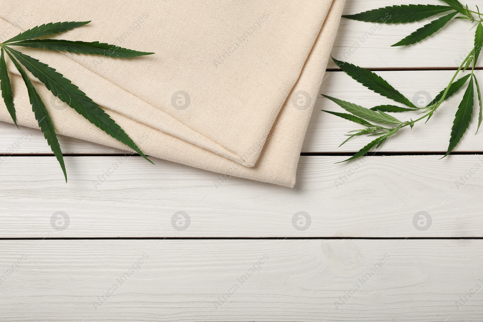 Photo of Hemp cloth and green leaves on white wooden table, flat lay. Space for text