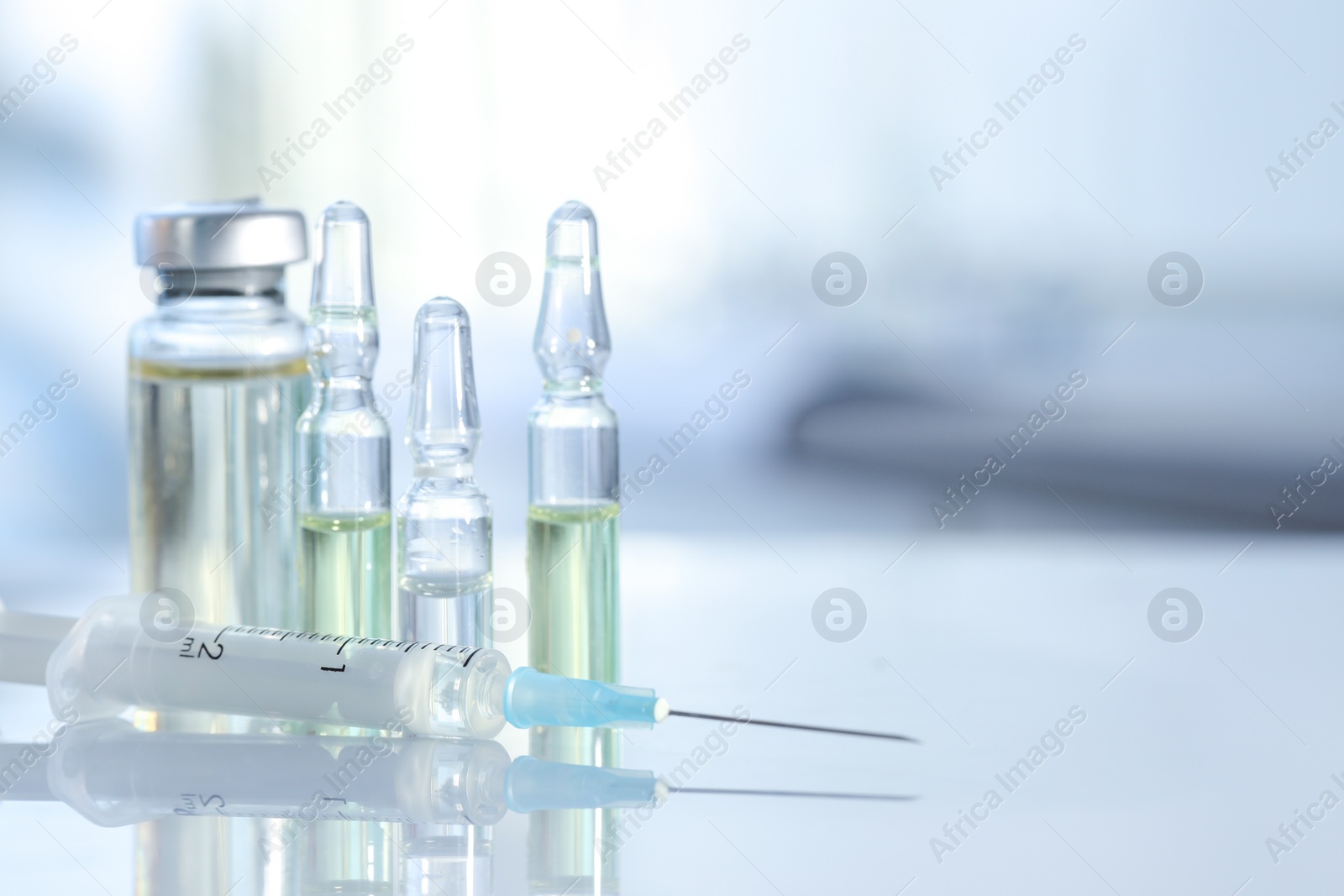 Photo of Glass vial, ampoules and syringe on white table, closeup. Space for text