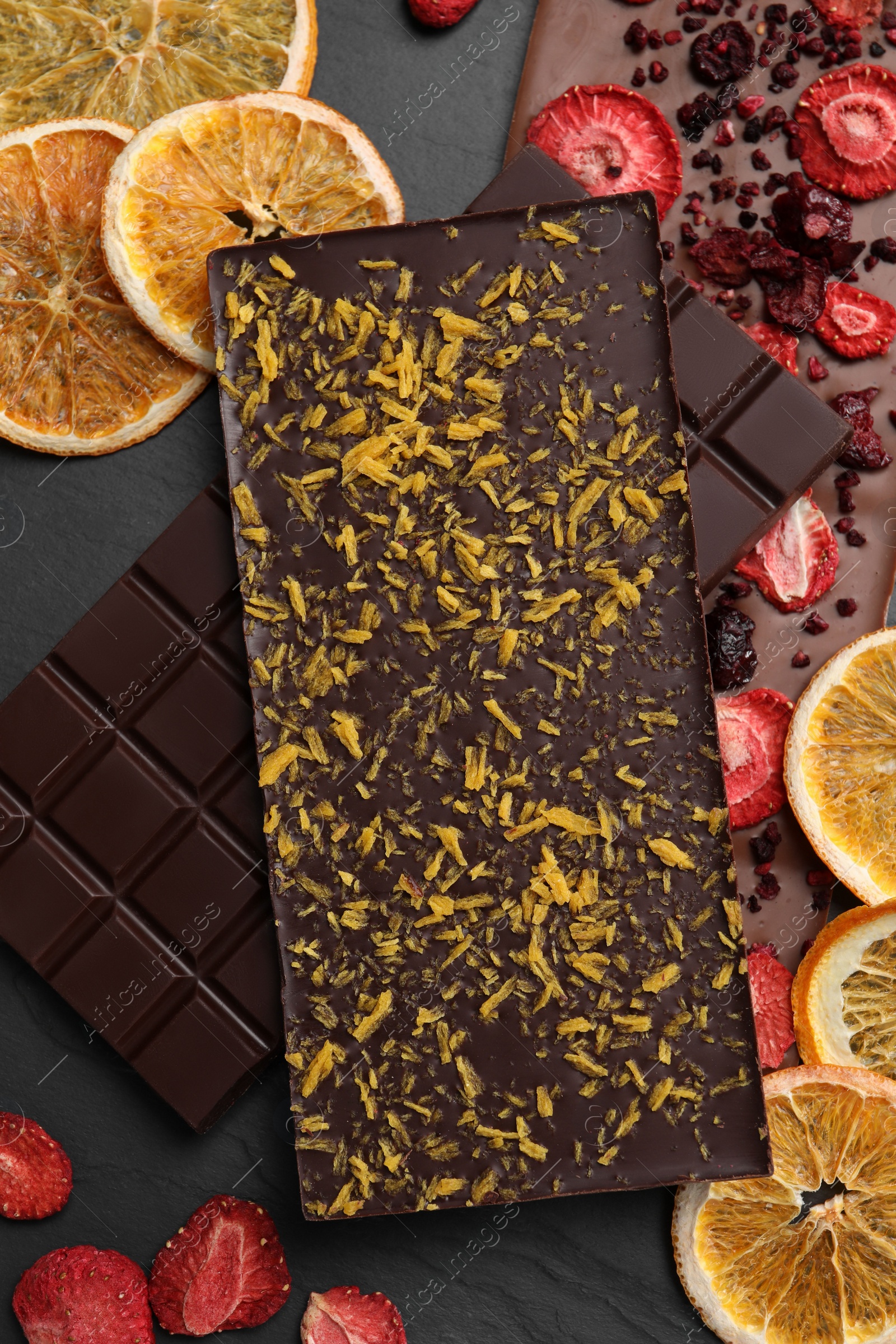 Photo of Different chocolate bars with freeze dried fruits on slate table, flat lay