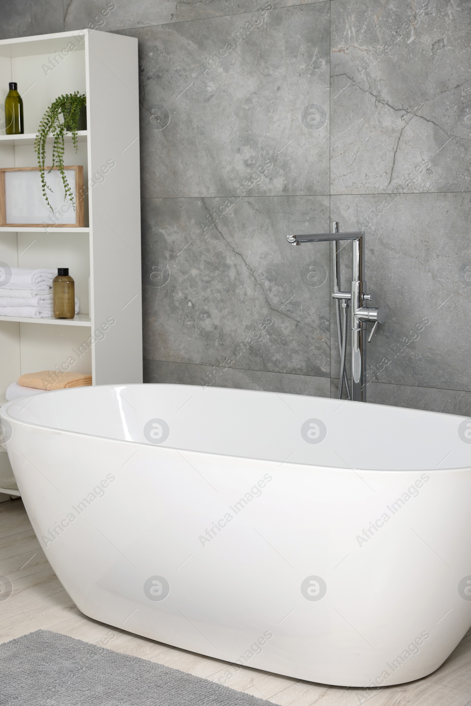 Photo of Stylish bathroom interior with ceramic tub, care products and towels in cabinet