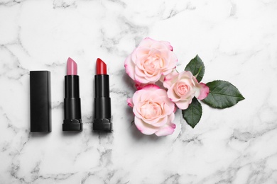 Photo of Different lipsticks and beautiful flowers on white marble table, flat lay
