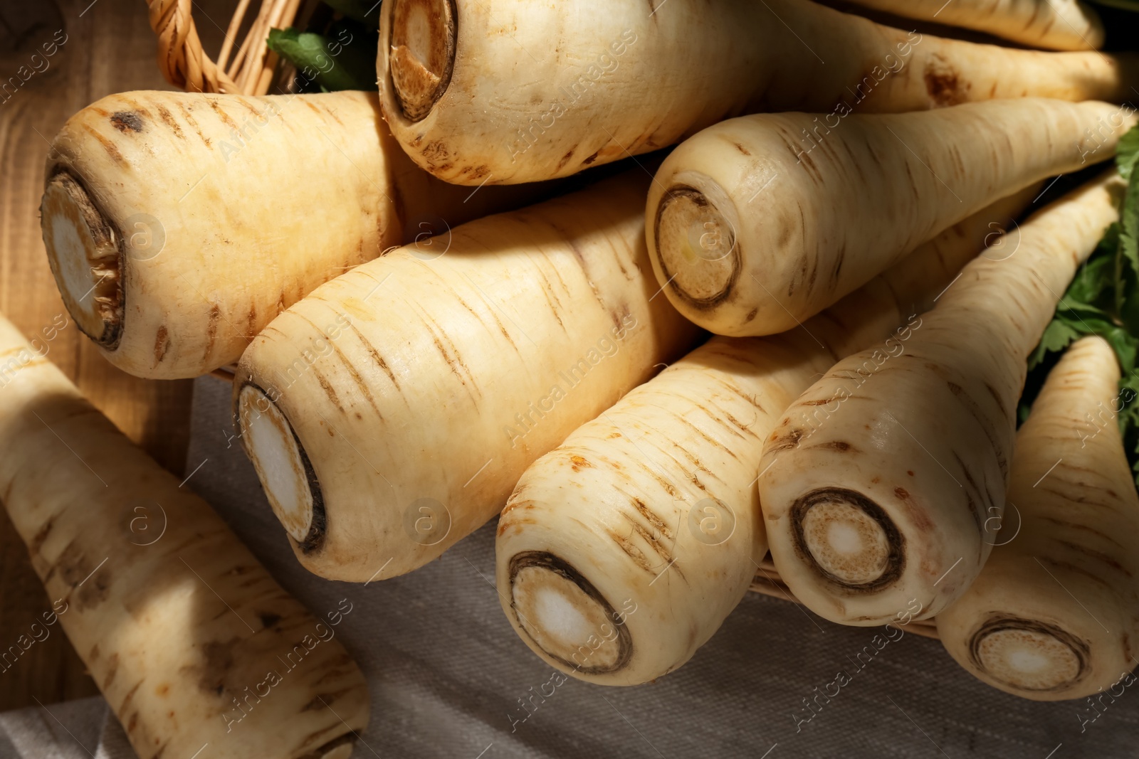 Photo of Wicker basket with delicious fresh ripe parsnips on wooden table, above view