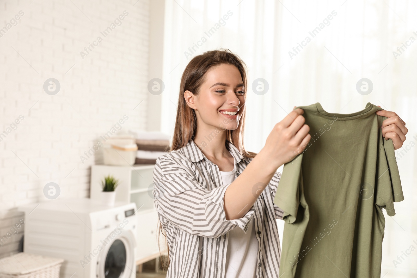 Photo of Happy young woman with clean t-shirt indoors. Laundry day